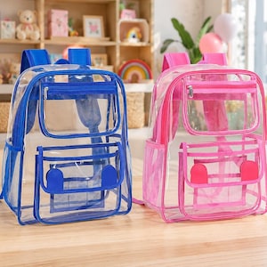 May include: Two transparent backpacks, one in blue and one in pink, each featuring a main zippered compartment, a smaller front zippered pocket, and two side mesh pockets. The front pockets have two rounded tabs, and the shoulder straps match the trim.