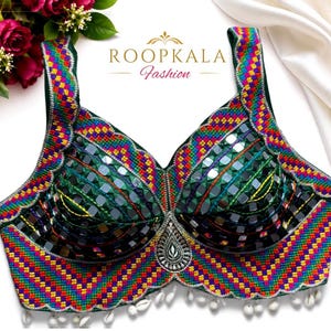 May include: A dark green sleeveless blouse featuring a vibrant, multi-colored geometric embroidered border, reflective mirror embellishments on the cups, a central teardrop-shaped mirror accent, and small white shell charms along the bottom hem.