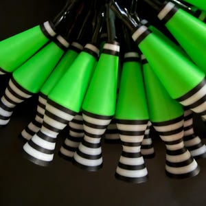 May include: A string of Halloween-themed lights featuring green conical bulbs and striped black and white bases. The lights are arranged against a dark background, creating a festive and eye-catching display.