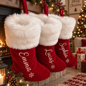 May include: Three red velvet Christmas stockings with white faux fur cuffs. Each stocking features a white embroidered name, Emma, Lucas, or Sophia, and a small white snowflake design near the toe. Each stocking has a red fabric hanging loop.