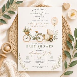 Puede incluir: Una tarjeta de invitación para baby shower con una bicicleta verde, una cesta de mimbre con vegetación y un sidecar. El texto dice: Our greatest adventure continues, we're thrilled to be adding one more to our crew, baby shower, Madison Smith, Saturday June 14 2025, 2:00 PM, The Hidden Oak Cafe, 123 Woodland Lane, Amazon and Target.