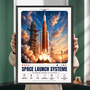 Könnte beinhalten: Ein gerahmtes Poster mit der NASA Space Launch System Rakete bei einem Start im Sonnenuntergang. Die Grafik enthält technische Daten wie eine Höhe von 98 M, einen Durchmesser von 8,4 M, eine Geschwindigkeit von 39.000 KM/H+ und 95.000 KG Nutzlast.