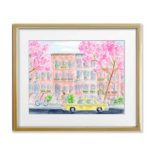 May include: Watercolor print of a New York City street scene with a yellow taxi, cherry blossom trees, and brownstone buildings. The artwork is framed in a gold-colored frame.