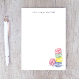 May include: A white notepad with the name "Monica Smith" printed at the top. The notepad has a watercolor illustration of a stack of colorful macarons in the bottom right corner.
