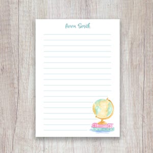 May include: Lined stationery with the name "Anna Smith" in light blue script at the top. A watercolor globe illustration sits on a stack of books in the bottom right corner. The globe is gold and the books are pink and blue.