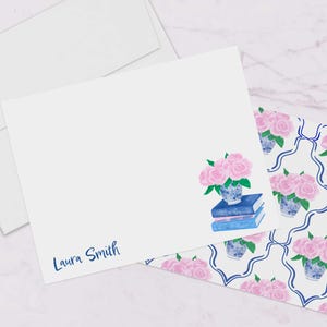 May include: White stationery with a blue and white floral pattern. The stationery has a pink floral illustration with a blue vase and books. The stationery is personalized with the name "Laura Smith".