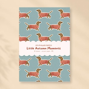 Pode incluir: Um pacote de papel autocolante com fundo azul e um padrão repetitivo de cães dachshund castanhos com camisolas às riscas vermelhas e brancas. A etiqueta central diz MYJOURNALPAGESS Little Autumn Moments 12 sheets - sticker paper - A5.