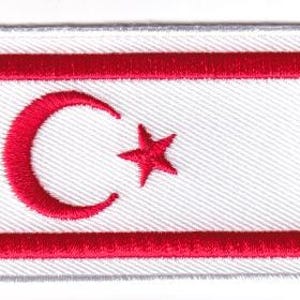 May include: A rectangular embroidered patch featuring a white background with two horizontal red stripes at the top and bottom. A red crescent moon and a five-pointed red star are centered between the two horizontal red stripes.