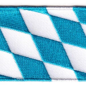 Könnte beinhalten: Ein rechteckiger gestickter Aufnäher mit einem sich wiederholenden Rautenmuster in abwechselnden Farbtönen von hellem Cyanblau und Weiß. Die Kanten des Aufnähers sind mit einem sauberen, weißen gestickten Rand versehen, der eine klare Form bildet.