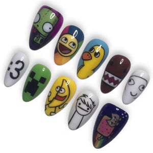 May include: A set of eleven almond-shaped press-on nails featuring various colorful cartoon and internet meme graphics, including a green alien, a yellow duck, a brown creature with sharp teeth, a banana, and a pixelated cat on a dark blue background.