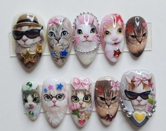 May include: A set of ten press-on nails featuring detailed cat portraits. The designs include cats wearing hats, sunglasses, glasses, and bows, accented with small 3D elements like stars, hearts, pearls, and flowers in various colors.