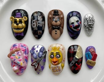 May include: A set of ten press-on nails featuring 3D character designs and motifs. The nails display a golden bear, a checkered pattern with 6AM text, a brown bear, a white mask, a silver skeleton hand, pizza, a guitar, a yellow bird with LET'S EAT text, a flashlight, and prize tickets.