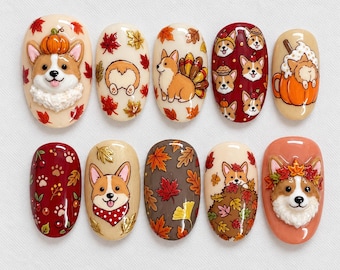 May include: A set of ten press-on nails featuring Corgi dog designs with autumn themes. The nails display various illustrations including Corgi faces, paw prints, pumpkins, and colorful fall leaves in shades of orange, red, brown, and cream.