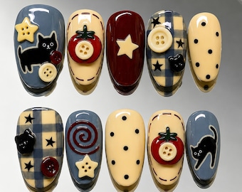 May include: A set of ten press-on nails featuring various designs including black cats, red tomatoes with button centers, cream stars, blue and cream plaid patterns, cream polka dots, and red spirals, accented with small plastic buttons.
