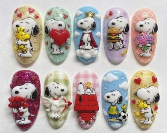 May include: Ten oval-shaped nail art charms featuring Snoopy and Woodstock in various scenes, including holding a heart, wearing a crown, eating a burger, holding flowers, shooting an arrow, sleeping on a red doghouse, and playing soccer.