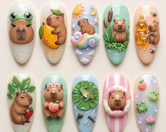 May include: A set of ten almond-shaped nail art tips featuring 3D-style capybara designs. The illustrations include a capybara with a frog hat, holding a lemon, sitting on a rainbow cloud, near cattails, with honey, eating a strawberry, holding a peach, near a frog on a lily pad, inside a striped floatie, and surrounded by small frogs and a lotus flower.