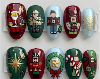 May include: A set of ten press-on nails featuring holiday designs including a block-style Santa, a nutcracker, a reindeer, a Roblox-inspired character, a wreath with an R, a candy cane, gold snowflakes, and various Christmas ornaments.
