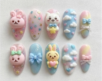 May include: A set of ten press-on nails featuring various designs including pink rabbit faces, blue bows, yellow rabbits holding hearts, white clouds, and pastel gradients. The nails are decorated with glitter, star-shaped sequins, and small bows.
