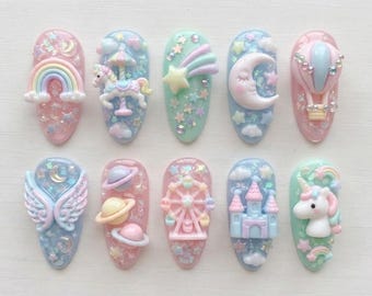 May include: Ten oval-shaped nail art charms featuring pastel-colored 3D designs including a rainbow, carousel horse, shooting star, crescent moon, hot air balloon, angel wings, planets, ferris wheel, castle, and unicorn, all with glitter accents.