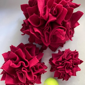 May include: Three red felt dog toys in the shape of a flower, with a yellow tennis ball in the center.