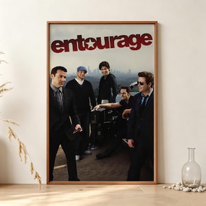 May include: A framed poster featuring the Entourage television show logo in red text at the top. Below the title, four men stand in a group against a city skyline background. The men are dressed in dark suits and casual attire, posing together.