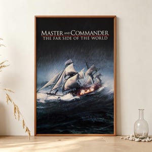 Puede incluir: Un cuadro rectangular con marco que muestra una escena oceánica oscura y tormentosa con un gran velero navegando sobre olas agitadas. El texto 'MASTER AND COMMANDER THE FAR SIDE OF THE WORLD' aparece en blanco y rojo sobre el fondo oscuro.