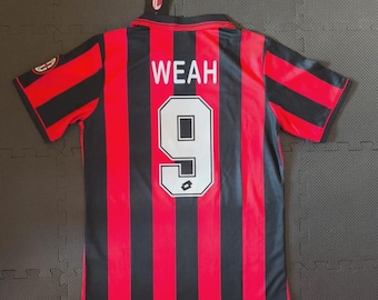 May include: A short-sleeved sports jersey featuring vertical red and black stripes. The back displays the name WEAH in white capital letters above the number 9 in a white font with a black outline. A small black tag is attached to the collar.