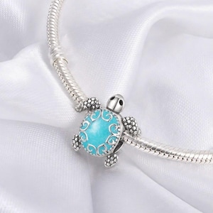 May include: A silver charm bead shaped like a turtle, featuring a bright turquoise blue oval centre with intricate silver filigree scrollwork overlay. The turtle has textured silver legs and a smooth head, threaded onto a flexible silver snake chain.