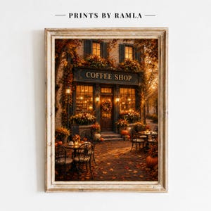 May include: A framed wall art print depicting a coffee shop storefront during autumn. The scene features warm golden lighting, orange foliage, and pumpkins scattered on the ground. The text COFFEE SHOP is displayed above the entrance door.