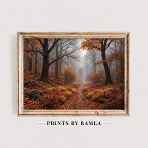 Könnte beinhalten: Ein gerahmter Landschaftsdruck, der einen Waldweg im Herbst mit orangefarbenem, rotem und braunem Laub, hohen Bäumen und einer nebligen Atmosphäre zeigt. Der Text PRINTS BY RAMLA ist unter dem Rahmen zentriert. Der Rahmen hat ein helles Holzfinish.