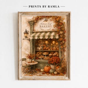 Puede incluir: Una lámina enmarcada titulada Autumn Leaf Bakery que muestra un escaparate con un toldo a rayas, una vitrina de pasteles, una mesa pequeña con una silla y calabazas. La escena está decorada con follaje otoñal y una lámpara de pared.