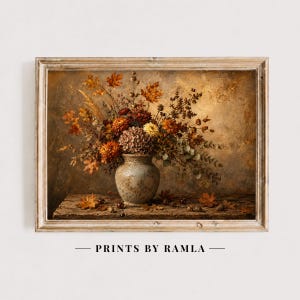 May include: A framed wall art print featuring a ceramic vase filled with dried autumn flowers and foliage in shades of orange, brown, and yellow. The arrangement sits on a wooden surface with scattered leaves. The text PRINTS BY RAMLA is visible.