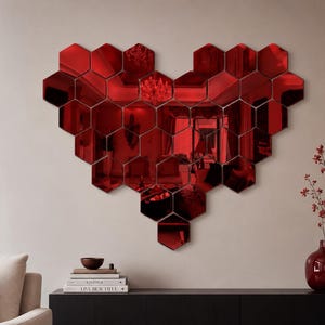 May include: A wall-mounted decorative arrangement of red hexagonal mirror tiles configured into a large heart shape. The reflective surfaces create a deep crimson tint, mirroring the surrounding room interior with a distinct red color cast throughout.