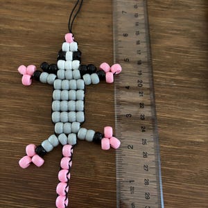 May include: A lizard-shaped keychain made of grey, black, and pink plastic pony beads on a black cord with a silver metal lobster clasp. A clear plastic ruler is placed next to the keychain, showing a total length of approximately 5.5 inches.
