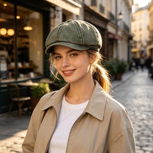 May include: A sage green newsboy cap with a structured crown and a short, curved brim. The cap features a multi-panel design with visible stitching along the seams, crafted from a soft, washed-out fabric that provides a textured appearance.