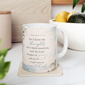 May include: A white ceramic mug featuring a watercolor coastal scene and the text Jeremiah 29:11, For I know the thoughts that I think toward you, saith the Lord, thoughts of peace, and not of evil, to give you an expected end.