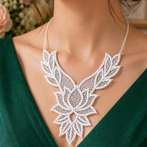 May include: A white lace necklace featuring an intricate floral lotus design with symmetrical leaf-like extensions. The piece is constructed from delicate, openwork embroidery and is attached to a thin, matching white chain that rests around the neck.