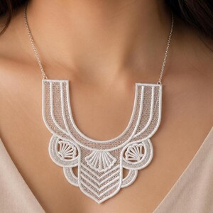 May include: A white lace statement necklace featuring an intricate, openwork geometric pattern with scalloped edges and fan-like motifs. The bib-style design is suspended from a thin, matching white chain that secures around the neck.