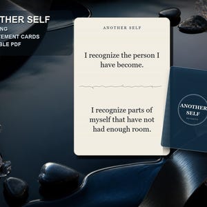 Op de afbeelding: Een crèmekleurige statementkaart met de tekst "ANOTHER SELF" bovenaan, gevolgd door de zinnen "I recognize the person I have become." en "I recognize parts of myself that have not had enough room." Een donkerblauwe kaart met een cirkelvormig logo ligt ernaast.