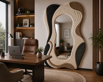 May include: A large, floor-standing mirror with an irregular, organic-shaped frame covered in textured, tufted fabric in shades of cream, beige, and black. The mirror reflects a home office interior with a desk, chair, and a framed sign on the wall.