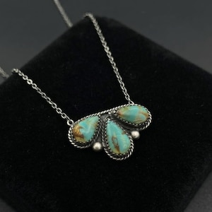 Può includere: Una collana in argento con un ciondolo composto da tre pietre turchesi a forma di goccia. Ogni pietra è incastonata in una cornice di filo d'argento intrecciato con piccole sfere d'argento tra loro. Il ciondolo è fissato a una sottile catena.