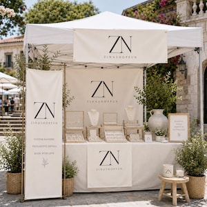 May include: A white pop-up canopy tent featuring the ZN ZINASHOPFUN logo on banners and a table skirt. The display includes jewellery stands, a large ceramic vase, potted greenery in woven baskets, and a small wooden stool with a branded candle.