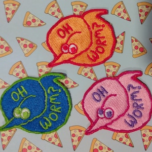 May include: Three embroidered patches in orange, blue, and pink, each with a cartoon worm design and the words "OH WORM?" in a speech bubble shape. The patches have googly eyes, set against a background of pizza slices.