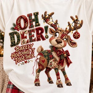 May include: A white t-shirt featuring a graphic of a reindeer with a plaid pattern, wearing a red bow, and tangled in string lights. The text reads "OH DEER! BARELY HOLDING IT TOGETHER" in red and green plaid lettering with decorative accents.