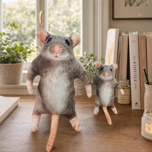 Puede incluir: Dos juguetes de peluche con forma de ratón con patrones de pelaje realistas en gris y blanco, narices rosadas y colas largas. El ratón más grande se encuentra en primer plano, mientras que una versión más pequeña está detrás, ambos de pie.