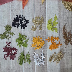 Könnte beinhalten: Eine Sammlung kleiner, ausgestanzter Papierformen in Form von Herbstblättern und Zweigen, angeordnet in zwölf verschiedenen Gruppen. Die Farben umfassen Schwarz, Gold, Limettengrün, Olivgrün, Dunkelrot, Senfgelb, Orange, Braun, Weiß und Beige.