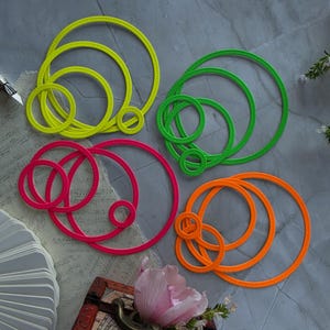 Puede incluir: Cuatro juegos de troqueles circulares de metal en colores amarillo neón, verde neón, rosa neón y naranja neón. Cada juego consta de varios anillos concéntricos con un detalle de borde cosido, organizados en cuatro grupos.