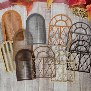 Könnte beinhalten: Eine Sammlung von gestanzten Fensterformen in verschiedenen Farben wie Orange, Grau, Braun und Gold. Das Set enthält bogenförmige Designs mit horizontalen Lamellen und bogenförmige Designs mit rautenförmigen Scheiben, die verstreut angeordnet sind.