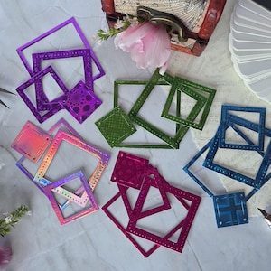 Puede incluir: Una colección de troqueles de corte metálicos cuadrados en varios colores, incluyendo morado, verde, azul, rosa y acabados iridiscentes. Cada troquel presenta un patrón de borde cosido decorativo a lo largo de los lados, diseñado para proyectos de manualidades.