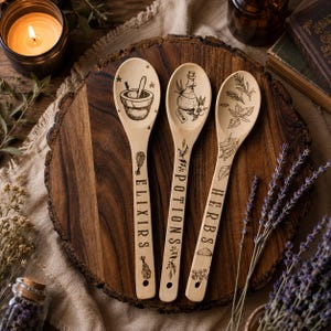 May include: Three light-colored wooden spoons featuring black laser-engraved illustrations and text. The first spoon displays a mortar and pestle with the word ELIXIRS. The second shows a potion bottle with POTIONS. The third features herbs with HERBS.